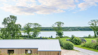 4-Sterne-Ferienhaus in Rønde mit Blick auf einen See, umgeben von Bäumen und grüner Naturlandschaft.