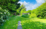 Jardin verdoyant avec chemin et arbustes fleuris au gîte pour 6 personnes à Bogense, Danemark, par temps ensoleillé.