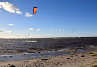 Kitesurfeurs sur la plage à Bogense, Danemark, profitant du beau temps sous un ciel bleu et clair.