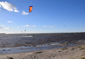 Kitesurfisti sulla costa vicino a Bogense, Danimarca, in una giornata soleggiata con cielo azzurro.