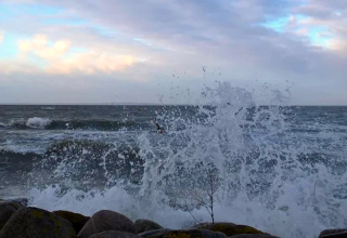 Vagues frappant les rochers près d'une maison de vacances pour 6 personnes à Bogense, Danemark, sous un ciel clair.
