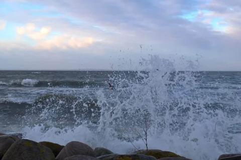 Golven slaan tegen de rotsen bij het 6-persoons vakantiehuis in Bogense, Denemarken, onder een heldere lucht.