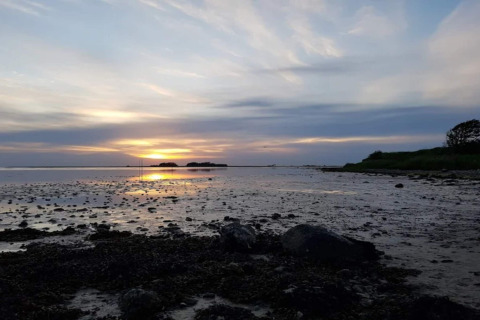 Solnedgang over lavvandet strand ved 6 personers feriehus i Bogense, Danmark, med skyer og vand.