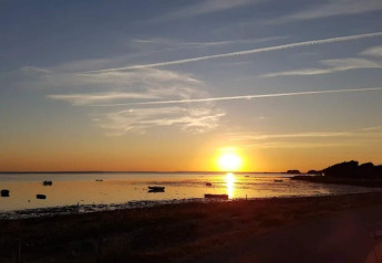Solnedgang over havet set fra 6 personers feriehus i Bogense, Danmark, med både og stille vand.