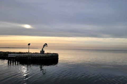 Vue sur la mer au coucher du soleil, avec une statue sur une jetée près d'une maison de vacances à Bogense, Danemark.