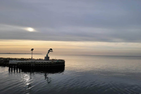 Udsigt over havet ved solnedgang, med en statue på en mole ved 6 personers feriehus i Bogense, Danmark.