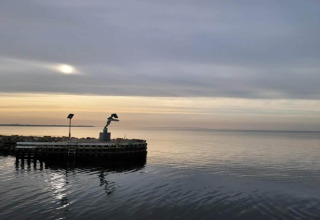 Vista del océano al atardecer con una estatua en un muelle cerca de una casa de vacaciones en Bogense, Dinamarca.