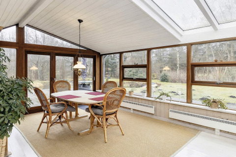 Luminoso comedor con ventanales y sillas de mimbre en casa de vacaciones para 6 personas en Bogense, Dinamarca.