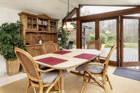 Salle à manger lumineuse dans une maison de vacances à Bogense, Danemark, avec chaises en osier et vue jardin.