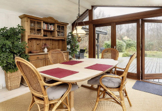 Salle à manger lumineuse dans une maison de vacances à Bogense, Danemark, avec chaises en osier et vue jardin.