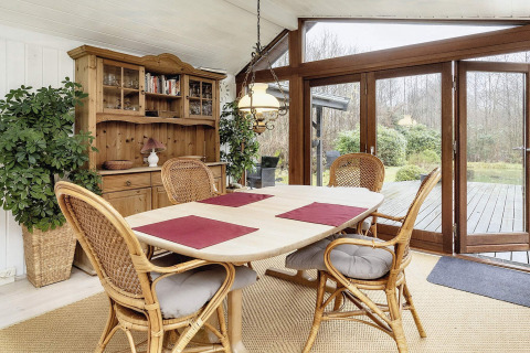Comedor luminoso en casa de vacaciones en Bogense, Dinamarca, con sillas de mimbre y vista al jardín.