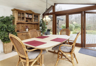 Lichte eetkamer in vakantiehuis in Bogense, Denemarken, met rotan stoelen en uitzicht op de tuin.