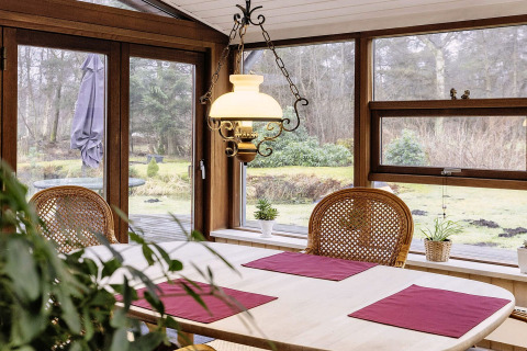 Salle à manger avec grandes fenêtres, meubles en bois et vue sur jardin dans maison de vacances à Bogense.