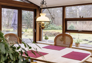Salle à manger avec grandes fenêtres, meubles en bois et vue sur jardin dans maison de vacances à Bogense.