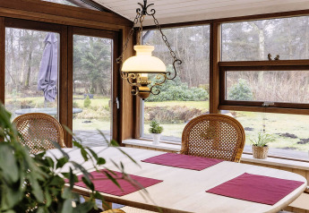 Salle à manger avec grandes fenêtres, meubles en bois et vue sur jardin dans maison de vacances à Bogense.