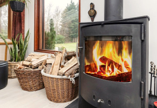Poêle à bois chaleureux avec paniers à bois près d'une fenêtre dans une maison de vacances à Bogense, Danemark.