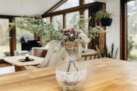 Bloemenboeket in glazen vaas op houten tafel in lichtrijke woonkamer van vakantiewoning in Bogense, Denemarken.