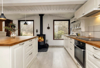 Cuisine lumineuse et chaleureuse dans une maison de vacances à Bogense, Danemark, avec poêle et grandes fenêtres.