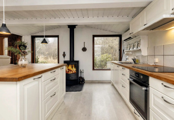 Cuisine lumineuse et chaleureuse dans une maison de vacances à Bogense, Danemark, avec poêle et grandes fenêtres.