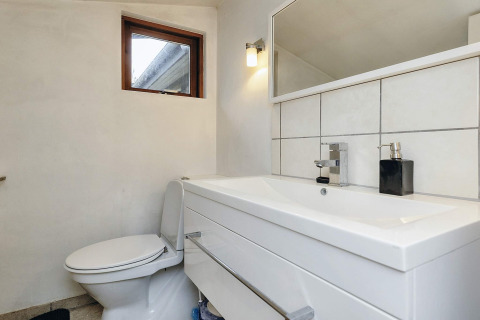 Moderne badkamer in een vakantiehuis in Bogense, Denemarken, met wastafel, toilet en spiegel aan de muur.