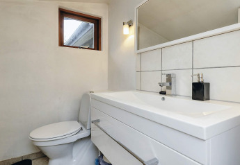Modern bathroom in a holiday home in Bogense, Denmark, featuring a sink, toilet, mirror, and wall light.