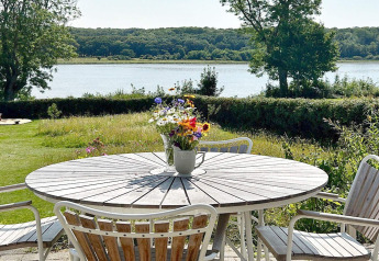 Table ronde en bois avec vase de fleurs et chaises sur terrasse avec vue sur lac à Rønde, Danemark.
