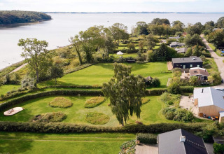 Luftaufnahme eines Ferienhauses in Rønde, Dänemark, nahe dem Wasser mit viel Grün und Bäumen.