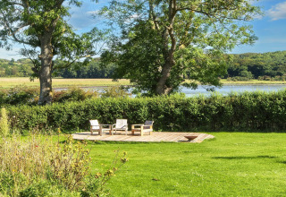 Terrazza in legno con tre sedie e giardino verde vicino al lago presso casa vacanze 4 stelle a Rønde, Danimarca.