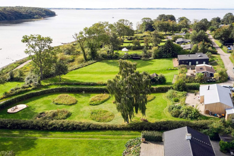 Luftfoto af et feriehus i Rønde, Danmark, med frodige grønne haver og udsigt til havet.
