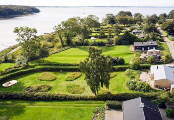 Luftfoto af et feriehus i Rønde, Danmark, med frodige grønne haver og udsigt til havet.