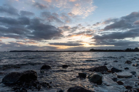 Küstenblick mit Steinen und Sonnenuntergang am Wasser beim 4-Sterne-Ferienhaus in Rønde, Dänemark.