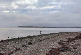 Una persona sola si trova su una spiaggia di ciottoli vicino all’acqua sotto un cielo nuvoloso a Rønde, Danimarca.