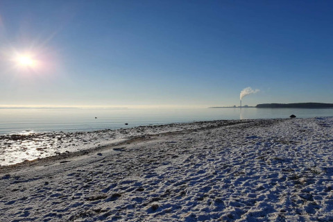 Zonnig winterstrand met sneeuw in Rønde, Denemarken. Rook van verre schoorsteen tegen blauwe lucht.