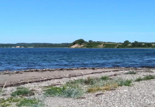 Vue sur l’eau et la plage depuis une maison de vacances 4 étoiles à Rønde, Danemark, avec ciel bleu.