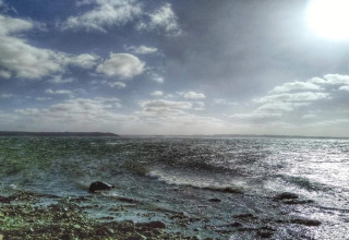 Coastal and sea view from 4 star holiday home in Rønde, Denmark, under a sunny sky with scattered clouds.