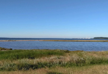 Vue d'une maison de vacances 4 étoiles à Rønde, Danemark, sur herbe, eau et industrie au loin sur l’horizon.