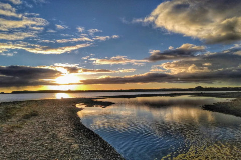 Coucher de soleil sur l’eau près du lodge « 4 star holiday home in Rønde » au Danemark, avec reflets et nuages.