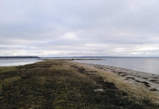Strandlandskab tæt på "4 stjernet feriehus i Rønde" i Danmark, med hav og himmel under skyer.
