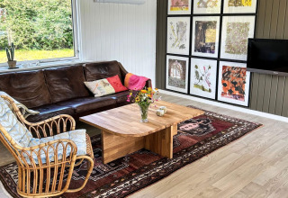 Sala en casa de vacaciones de 4 estrellas en Rønde, Dinamarca, con sofá de cuero y arte en la pared.