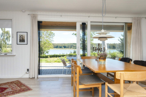 Salle à manger avec grandes fenêtres et vue sur le lac dans maison de vacances 4 étoiles à Rønde, Danemark.