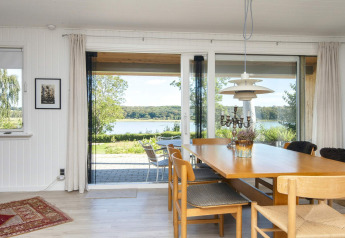Salle à manger avec grandes fenêtres et vue sur le lac dans maison de vacances 4 étoiles à Rønde, Danemark.