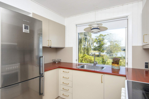 Cocina moderna con encimera roja, nevera de acero y gran ventana con vista a la naturaleza en Rønde.