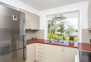 Moderne keuken met rood werkblad, inox koelkast en groot raam met uitzicht op groen in Rønde.