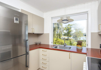 Moderne keuken met rood werkblad, inox koelkast en groot raam met uitzicht op groen in Rønde.
