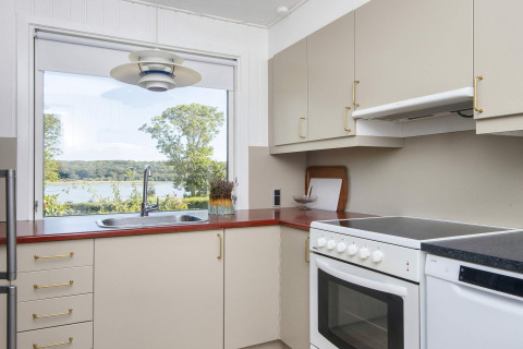 Moderne keuken met groot raam en uitzicht op meer en bos in 4-sterren vakantiehuis in Rønde, Denemarken.