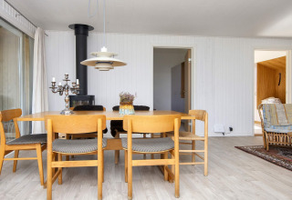 Eethoek in vakantiehuis in Rønde, Denemarken, met houten tafel, zes stoelen en houtkachel.