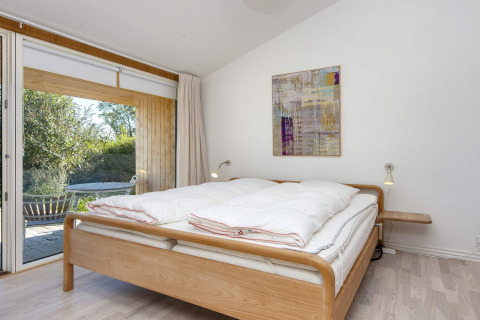 Lichte slaapkamer met dubbel bed, moderne kunst aan de muur en terras in een vakantiehuis in Rønde.