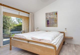 Lichte slaapkamer met dubbel bed, moderne kunst aan de muur en terras in een vakantiehuis in Rønde.