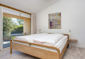 Lichte slaapkamer met tweepersoonsbed, moderne wandkunst en toegang tot het terras in Rønde, Denemarken.