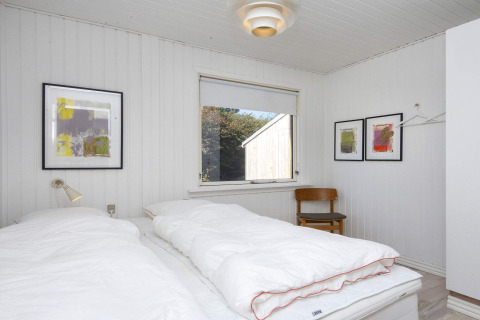 Camera con letti singoli, pareti bianche, arte moderna e sedia in una casa vacanze a Rønde, Danimarca.
